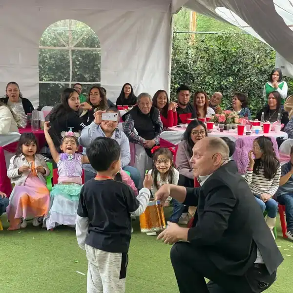 Fiesta familiar bajo carpa en jardín con el mago entre los invitados