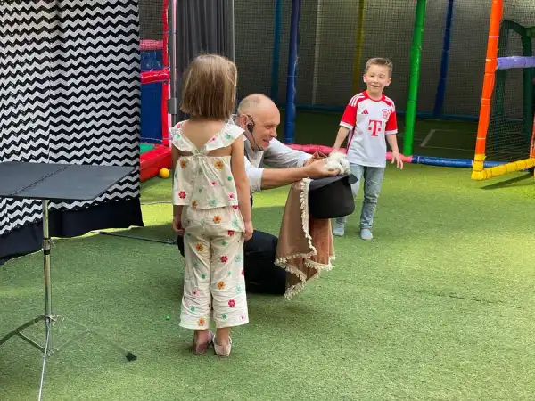 El mago muestra un conejito dentro del sombrero de copa a dos niños encantados